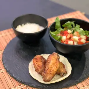 "Plato de alitas de pollo en freidora de aire, doradas y crujientes, servidas con salsa."